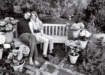 Pareja sentada en un banco de jardín rodeada de macetas y flores en una fotografía en blanco y negro