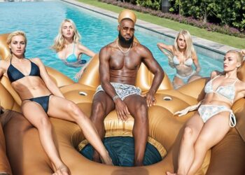 Hombre atlético sentado en un flotador dorado en la piscina rodeado de cuatro mujeres en bikini