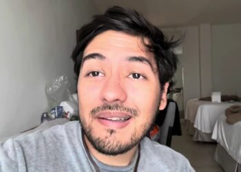 Hombre joven con barba y brackets en primer plano dentro de una habitación doble de hotel