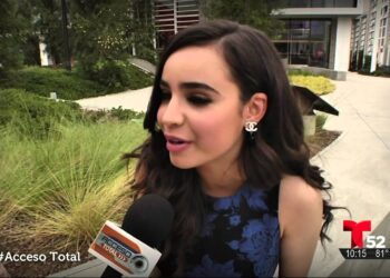 Joven siendo entrevistada al aire libre con micrófono y logo del canal