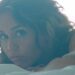 Mujer recostada en cama mirando a la cámara con luz suave y tatuajes visibles