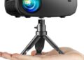 Proyector, ELEPHAS 2024 WiFi Mini proyector, 15000 Lux 1080P HD Proyector portátil Compatible con iOS/Android/Tablet/HDMI/TV Stick/USB (trípode incluidos) montado en un trípode pequeño y sostenido en la palma de la mano.