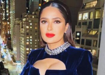 Actriz o celebridad en balcón nocturno con vestido azul de terciopelo, collar de brillantes y labios rojos, vista urbana iluminada