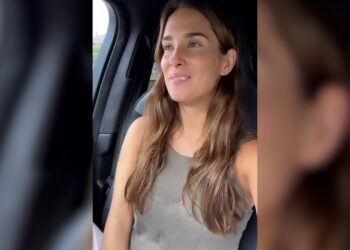 Mujer joven sonriente sentada en el asiento delantero de un coche, mirando hacia la ventana con luz natural.