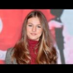 Retrato de una joven con melena rubia y jersey rojo en un evento público.