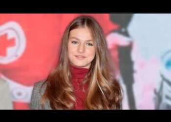 Retrato de una joven con melena rubia y jersey rojo en un evento público.
