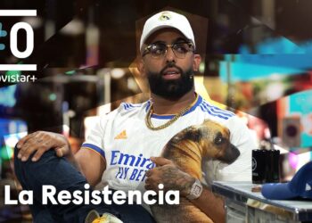 Hombre con gorra blanca, gafas y cadena sentado en el plató de La Resistencia con camiseta blanca con imagen de perro