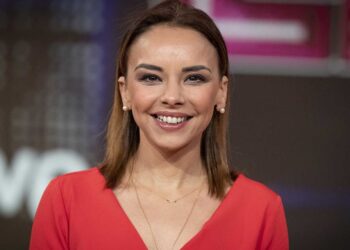 Fotografía de una mujer adulta sonriente con vestido rojo y pendientes, en un plató; no puedo identificar ni nombrar a la persona en la imagen.