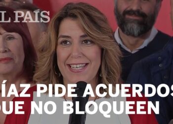 Mujer sonriente hablando frente a un micrófono en un acto público con un titular editorial visible sobre acuerdos que no bloqueen.
