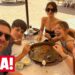 Familia sonriente compartiendo una paella en una terraza de playa EmgvBdD7aBw