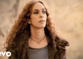 Retrato de una mujer de cabello rizado en exterior con mirada pensativa y aire de artista