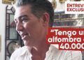 Hombre en perfil durante una entrevista en interior con texto superpuesto que dice 'Tengo una alfombra de 40.000€' y rótulo 'Entrevista exclusiva', expresión sonriente y ambiente doméstico