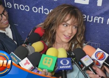 Mujer sonriente rodeada de micrófonos en una entrevista con diversos medios de comunicación.