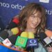 Mujer sonriente rodeada de micrófonos en una entrevista con diversos medios de comunicación.