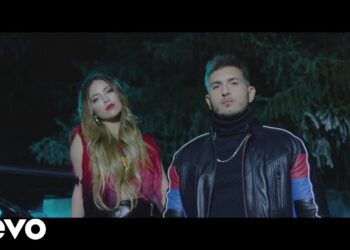 Dos artistas posando de noche frente a un vehículo con iluminación azul y el logo Vevo