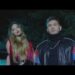 Dos artistas posando de noche frente a un vehículo con iluminación azul y el logo Vevo