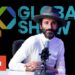 Artista sentado en un estudio frente a un micrófono y el logo 'Global Show' de fondo.