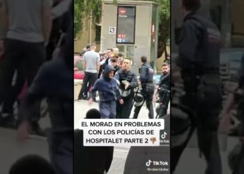 Policías rodean a un joven con capucha en una calle urbana mientras transeúntes observan, Dónde vive Morad: descubre el barrio que lo inspira y define