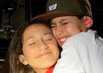 Dos niños sonrientes abrazándose en un escenario, mostrando ternura y complicidad, sin identificar a las personas