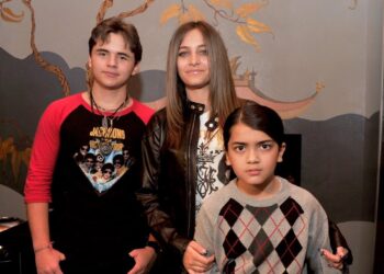 Tres jóvenes posan juntos en un interior frente a la cámara: dos adolescentes y un niño con ropa casual y expresiones neutras.