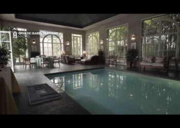 Piscina cubierta en salón señorial con grandes ventanales y mobiliario clásico