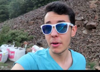 Joven con gafas de sol blancas y cristales azules frente a un talud rocoso y sacos de obra; Descubre dónde vive TheGrefg y la polémica de su casa en Andorra