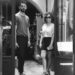 Dos adultos de pie en la entrada de una tienda en blanco y negro, estilo urbano con gafas de sol