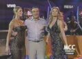 No puedo confirmar identidades; imagen de un programa de televisión en vivo con dos mujeres con vestidos elegantes y un hombre entre ellas.