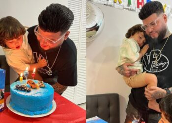 Hombre con su hijo soplando velas sobre una tarta azul decorada con coches de juguete