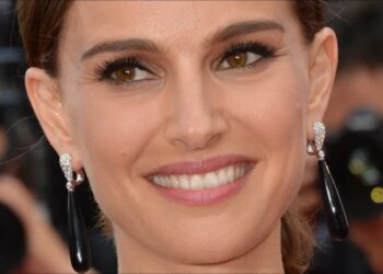 Primer plano de una actriz sonriente en la alfombra roja con pendientes largos negros y maquillaje elegante