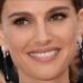 Primer plano de una actriz sonriente en la alfombra roja con pendientes largos negros y maquillaje elegante