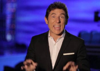 Hombre con traje sonriendo en plató televisivo, gesto entusiasta y fondo azul