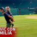 Hombre corriendo por la pista de césped con una niña a la espalda en un estadio de tenis, mostrando un instante íntimo de vida familiar.