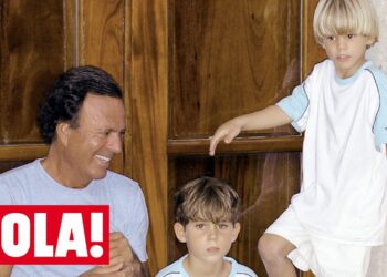 Padre sonriente con dos niños pequeños frente a una puerta de madera en interior