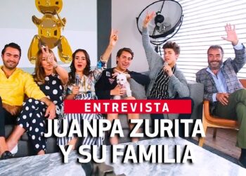 Grupo familiar sonriente en sofá durante una entrevista con micrófonos y un perro, UZmLNsNwFrs.