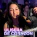 Mujer sonriente en la primera fila de un concierto sosteniendo una máscara junto a una valla y texto promocional, ¿Cuánto cobra Ulises Bueno por sus shows? Descubre su caché real