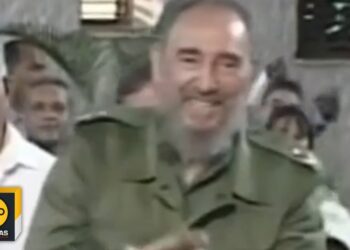 Hombre mayor con barba y chaqueta militar verde sonriendo en un evento público
