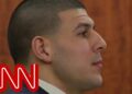 La familia de Aaron Hernández: secretos, tragedia y legado oculto 18 Perfil de un hombre con cabeza rapada en una sala de tribunal y el logo de una cadena de noticias en la esquina