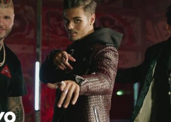 Dónde vive este artista: descubre su hogar y estilo de vida con tres hombres de estilo urbano vestidos con chaquetas de cuero y joyería, señalando a cámara en un set iluminado.