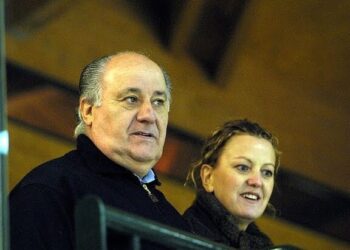 Hombre mayor y mujer junto a una barandilla observando un evento desde una grada