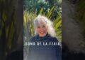 Mujer madura sonriente con cabello rizado y canoso frente a vegetación, con el texto visible 'DOMO DE LA FERIA'.