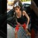 Mujer saliendo de un coche en una calle empedrada con pañuelo en la cabeza, tatuajes visibles y un cigarrillo en la mano.
