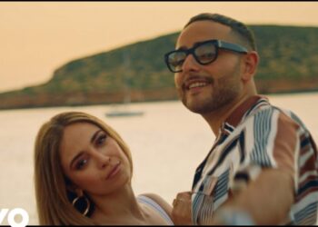 Pareja posando en la orilla al atardecer en un videoclip musical con logo Vevo visible