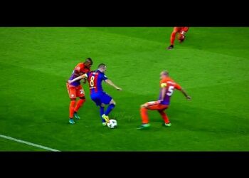 Jugador con camiseta azulgrana y dorsal 8 driblando entre dos rivales con camisetas naranjas sobre césped de estadio