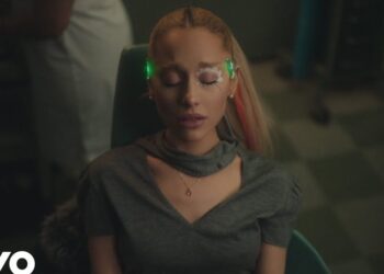 Mujer joven con los ojos cerrados, maquillaje en las pestañas y pequeños dispositivos LED verdes colocados en las sienes mientras está sentada en una silla.