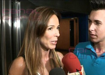 Mujer con cabello largo habla ante micrófonos rojos mientras un hombre la escucha asqR8jahe3s