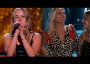 Joven cantante en primer plano con micrófono y dos mujeres sonrientes detrás en un escenario iluminado