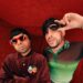 Dos músicos con gafas de sol y ropa llamativa en un set rojo, De dónde es Bad Bunny: descubre sus raíces puertorriqueñas.