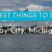 Panorámica del frente marítimo de Bay City, Michigan con texto promocional de actividades y logo; ¿De dónde es Madonna? Descubre su origen y legado musical.