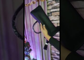 Descubre por qué todas las influencers llevan este bolso de 39 euros y no podrás resistirte a tenerlo, clutch negro rectangular de mano con acabado liso sostenido por una mano frente a una decoración festiva